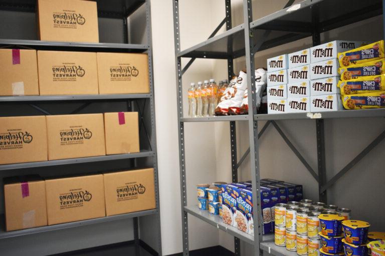 图为塔玛夸中心食品储藏室的货架上排列着各种包装好的商品和帮助收获的盒子.